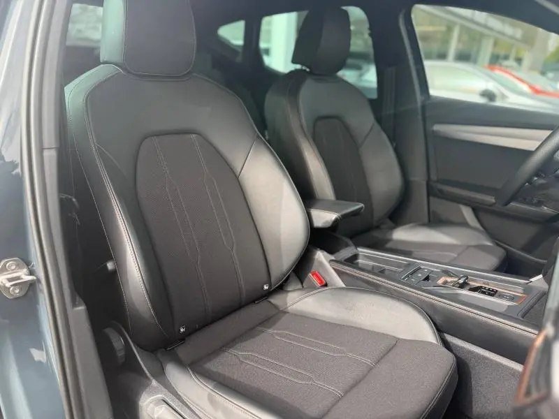 Vue intérieure côté avant gauche du CUPRA Formentor bleu 2025, sièges sport en textile noir avec accoudoir central.