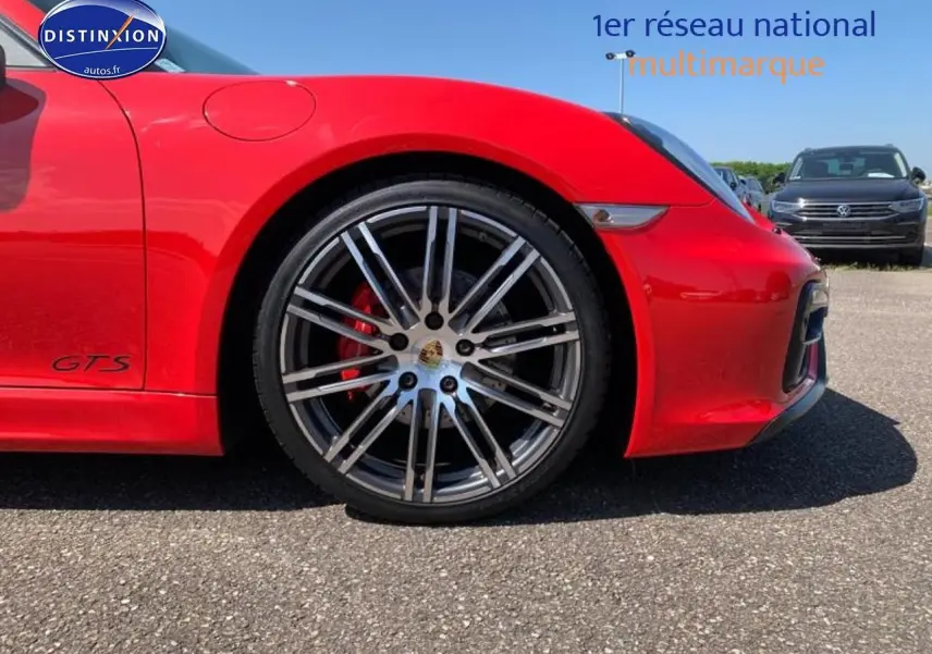 Gros plan sur la roue avant droite rouge d'une Porsche Boxster GTS avec jante alu et logo Porsche visible.