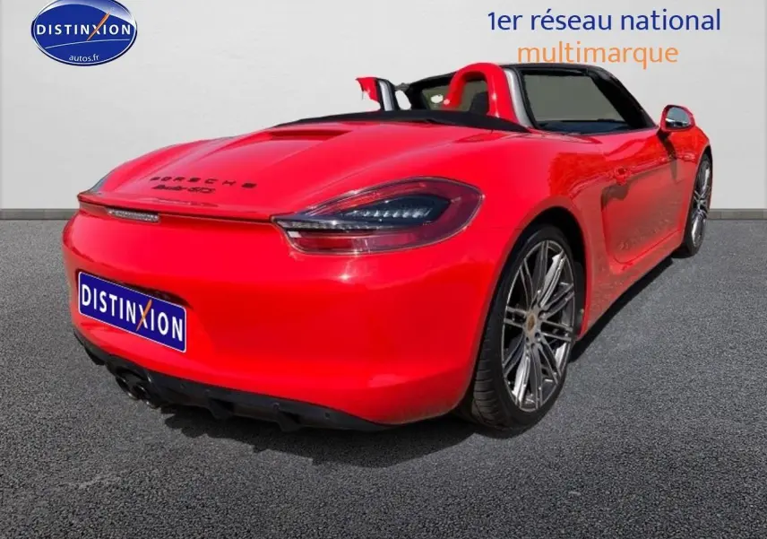 Vue 3/4 arrière droite d'une Porsche Boxster 981 rouge cabriolet avec jantes alu et becquet arrière.