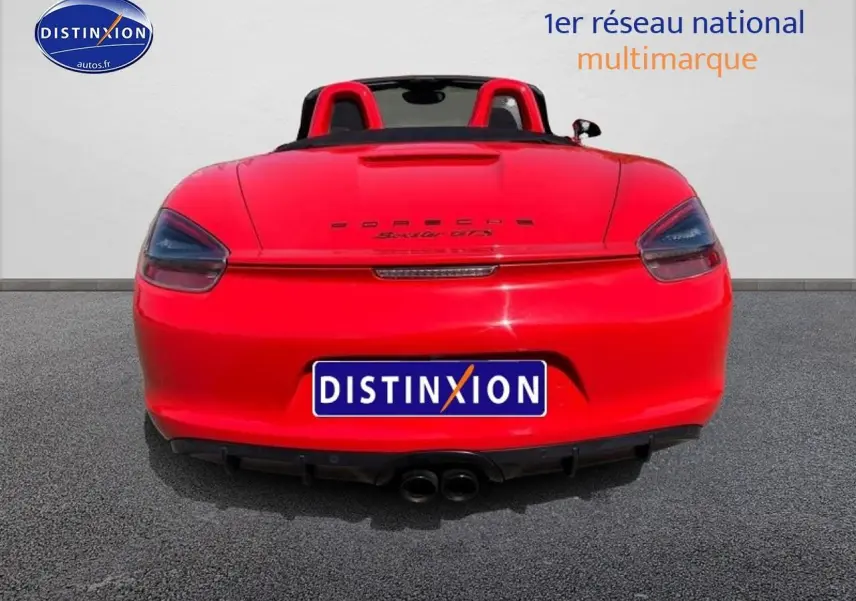 Vue arrière d'une Porsche Boxster GTS rouge cabriolet avec double sortie d'échappement et capote ouverte.