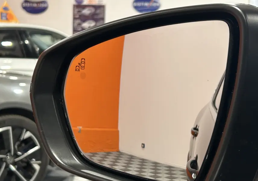 Rétroviseur côté droit montrant une partie du véhicule gris platinium métal et un mur orange en arrière-plan.