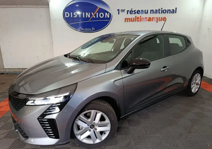 Renault Clio Evolution Blue dCi 100 gris clair vue 3/4 avant droit avec phares LED allumés en intérieur showroom.