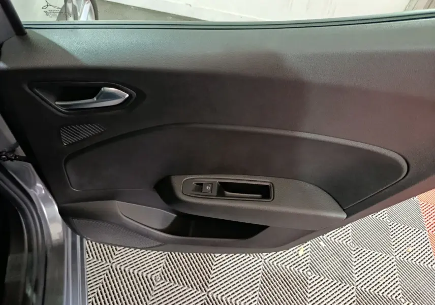 Vue intérieure de la porte côté gauche d’une Renault Clio gris clair, avec poignée argentée et commande de fenêtre.