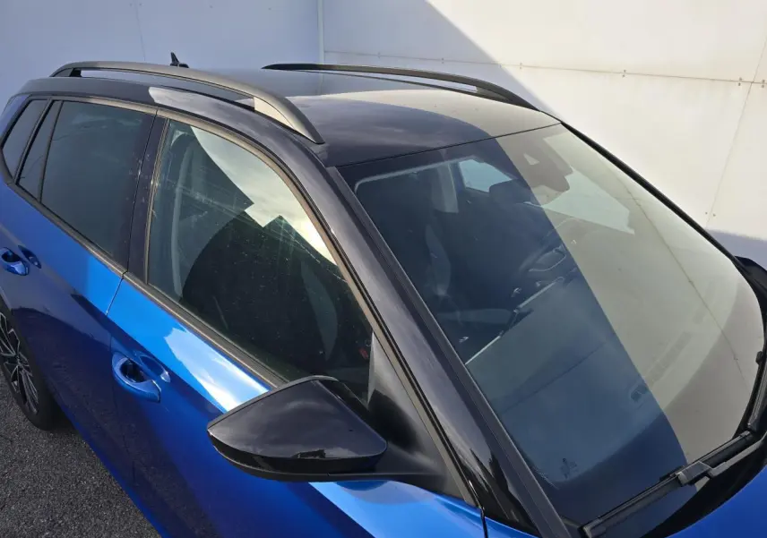 Vue 3/4 avant gauche d'un Skoda Kamiq 2025 bleu racing avec toit noir et barres de toit visibles.