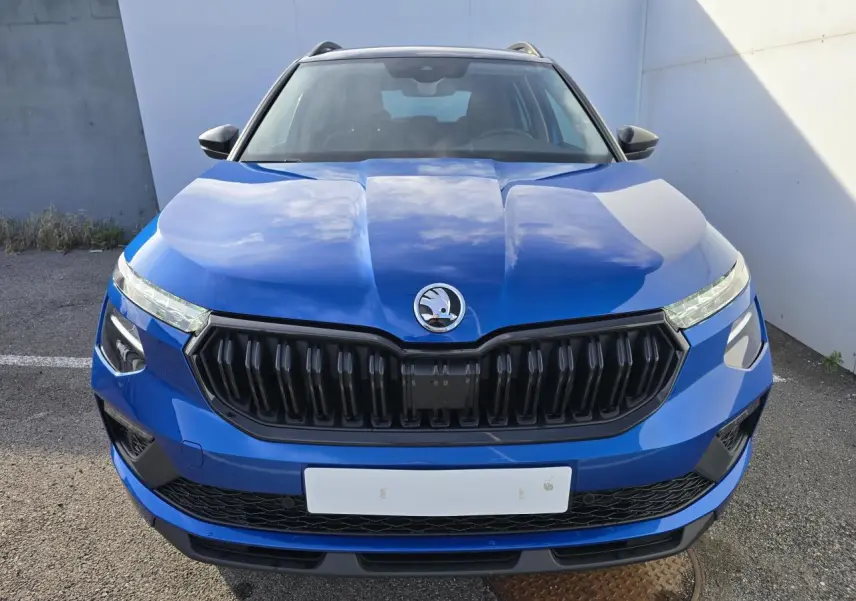 Vue frontale d'un Skoda Kamiq bleu racing avec calandre noire et toit noir visible en arrière-plan.