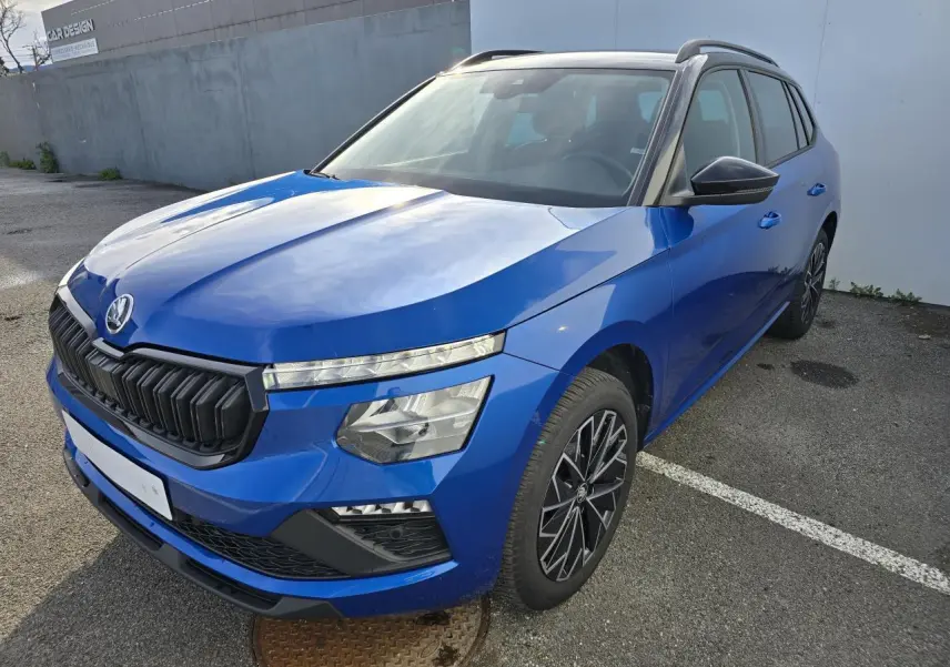Vue 3/4 avant d’une Skoda Kamiq bleu racing avec toit noir et jantes alliage 17 pouces, stationnée sur un parking.