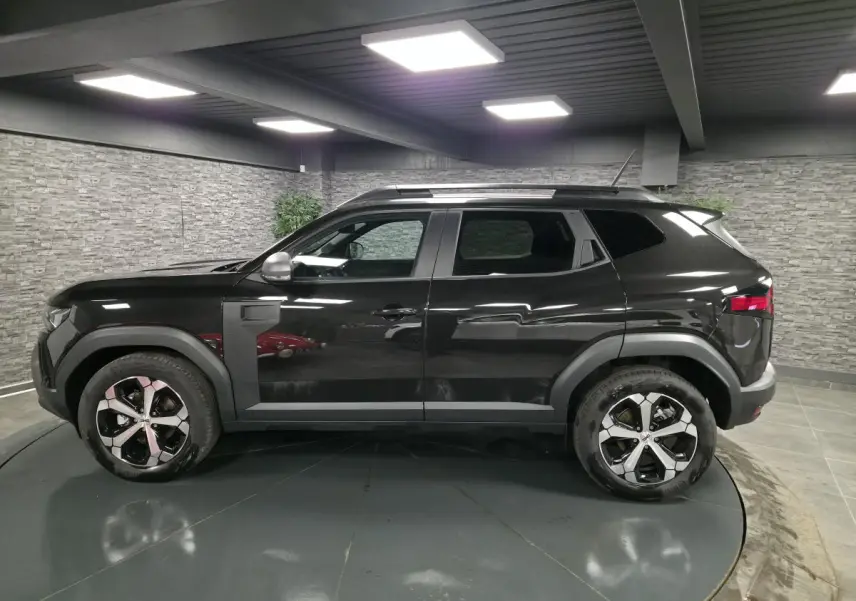 Profil côté gauche du Dacia Duster 1.6 Hybrid noir nacré, avec jantes alliage 18" diamantées et barres de toit noires.