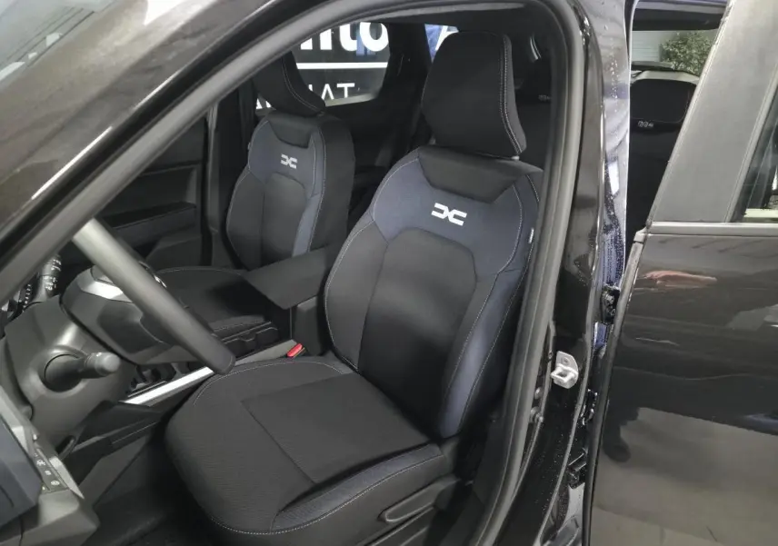 Vue intérieure côté conducteur du Dacia Duster 1.6 Hybrid 2025 noir nacré, sièges Denim bleu avec logo DC brodé.