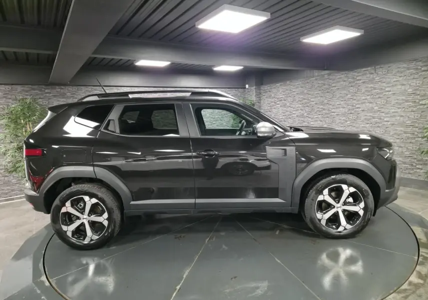 Vue de profil côté gauche du Dacia Duster 1.6 Hybrid noir nacré avec jantes alliage 18 pouces diamantées dans un showroom.