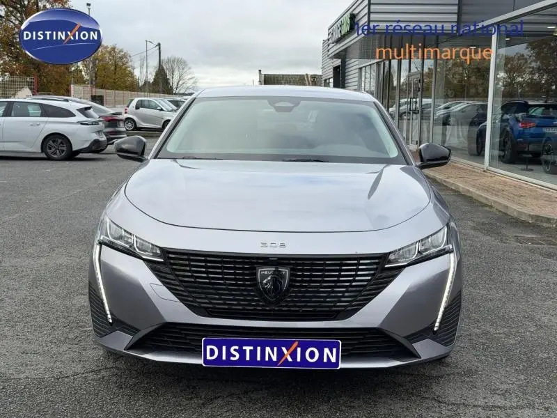 Vue avant d'une Peugeot 308 gris métallisé 2024 avec calandre noire et feux LED verticaux allumés.