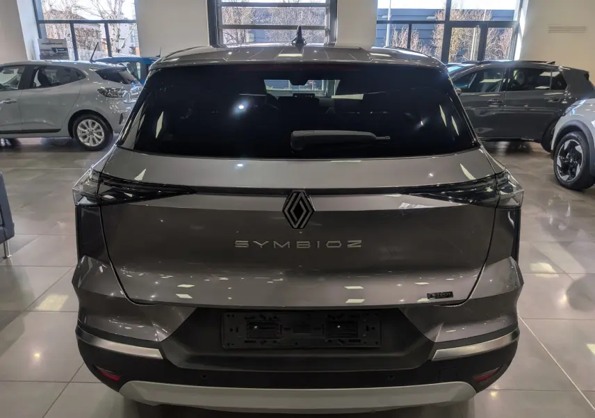 Vue arrière d'une Renault SYMBIOZ gris Cassiopé avec logo central et feux arrière étirés en intérieur showroom.