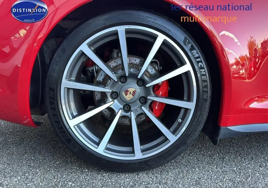 Gros plan sur la jante alu grise et le frein rouge d’une Porsche 911 Carrera 4 rouge côté arrière droit.