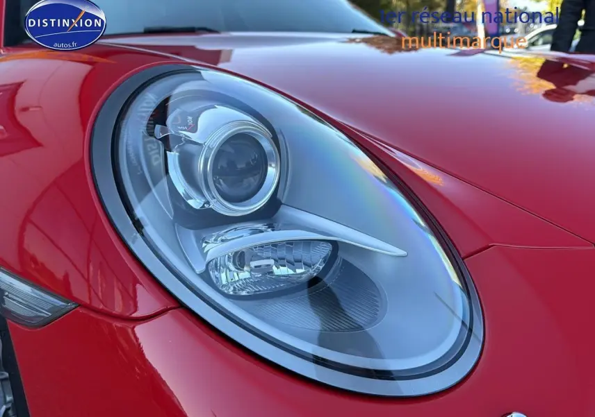Gros plan sur le phare avant gauche d’une Porsche 911 rouge (991) Carrera 4 PDK de 2013 avec carrosserie brillante.
