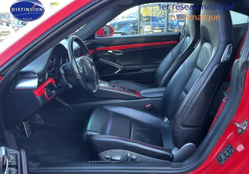 Vue intérieure côté conducteur d'une Porsche 911 rouge avec sièges cuir noirs et détails rouges sur tableau de bord.