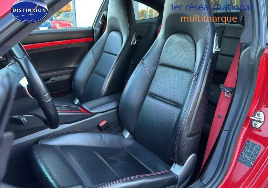 Vue intérieure côté conducteur de la Porsche 911 rouge, sièges cuir noir avec surpiqûres rouges et ceinture rouge visible.