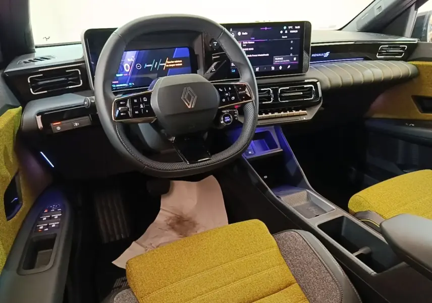Vue intérieure avant de la Renault R5 électrique 2024, sièges jaunes, tableau de bord avec écran tactile et volant multifonctions.