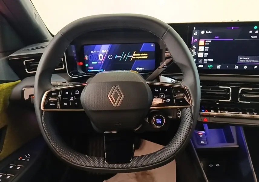 Vue frontale du volant noir perforé de la Renault R5 électrique 2024 avec tableau de bord numérique et écran tactile.