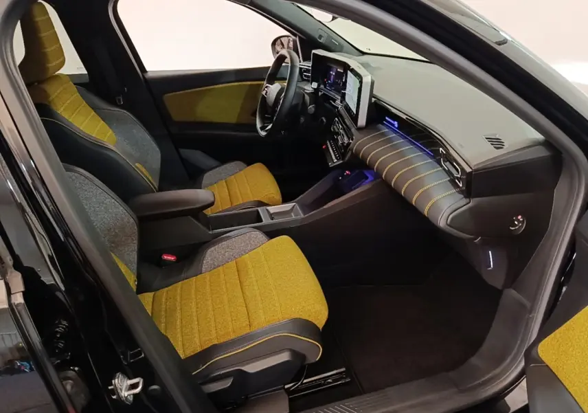 Vue intérieure côté conducteur de la Renault R5 Iconic 2024 avec sièges jaunes et tableau de bord moderne noir.