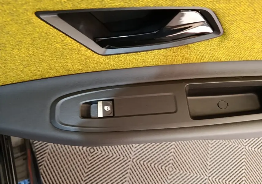 Gros plan sur la poignée intérieure noire et le bouton de verrouillage sur la porte côté gauche avec un revêtement jaune.