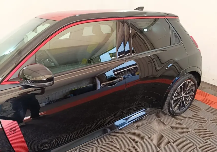 Vue latérale droite d'une Renault R5 électrique 2024 noire avec toit et détails rouges, jantes alliage noires.