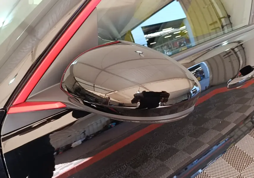Gros plan sur le rétroviseur côté gauche noir brillant avec cadre rouge d'une Renault R5 électrique 2024.
