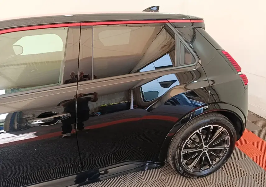 Vue latérale droite arrière d'une Renault R5 électrique 2024 noire avec jantes alliage et bande rouge décorative sur la vitre.