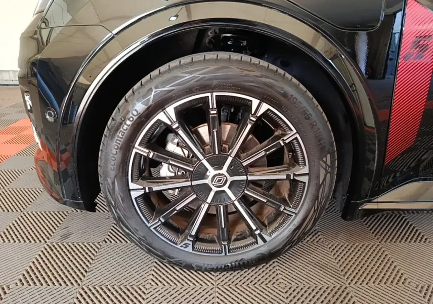 Gros plan sur la roue avant droite noire avec jante alliage bicolore et détail rouge sur la carrosserie.