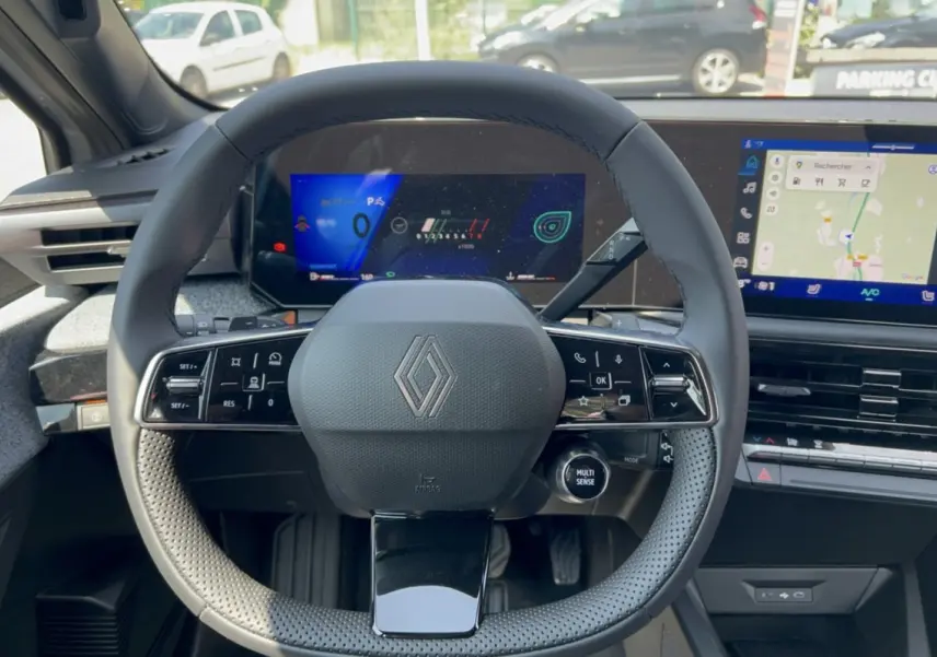 Vue intérieure centrée sur le volant multifonctions de la Renault Clio gris rafale avec tableau de bord numérique et écran tactile.