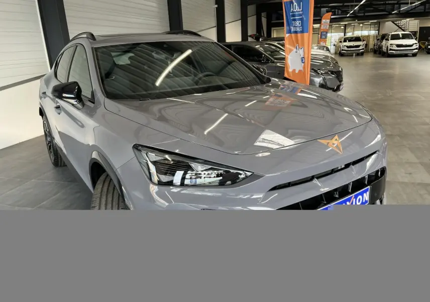 Vue 3/4 avant d'une CUPRA Formentor gris clair avec logo cuivré et rétroviseurs noirs dans un showroom.