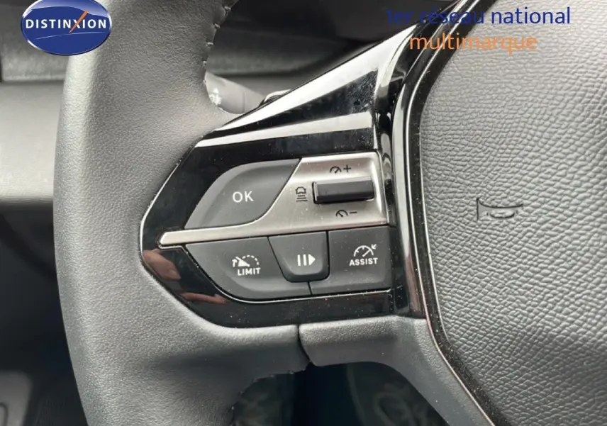 Gros plan sur les commandes du volant noir de la Peugeot 408 1.2 Hybrid 2025, avec boutons de régulateur et limiteur de vitesse.