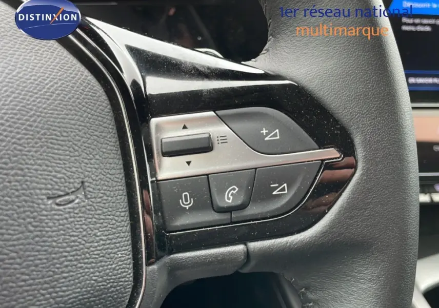 Gros plan sur les commandes multifonctions à gauche du volant en cuir noir du Peugeot 408 gris Selenium 2025.