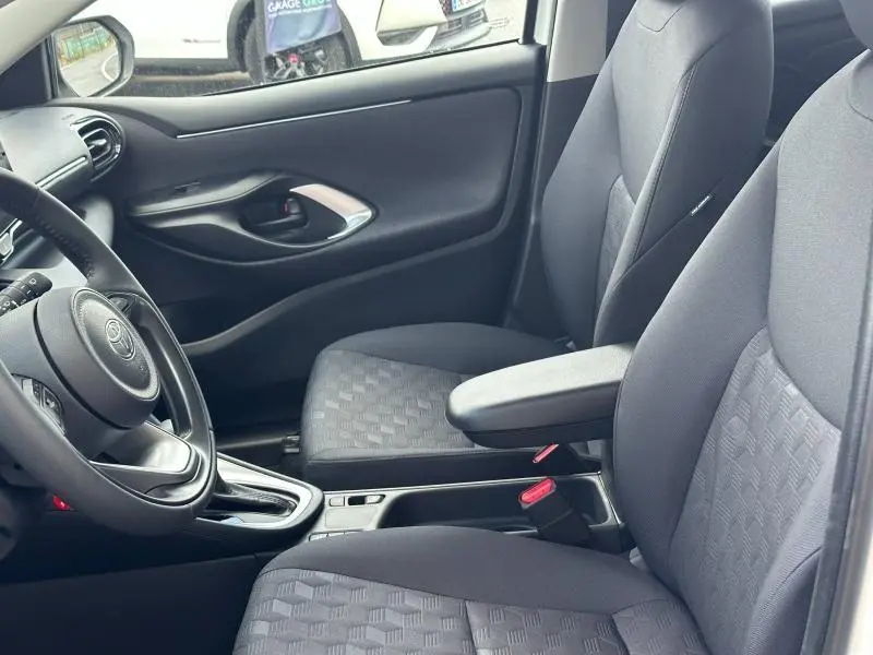 Intérieur de la Toyota Yaris 116h Dynamic 5p 2025 vu côté gauche, sièges tissu gris avec accoudoir central.