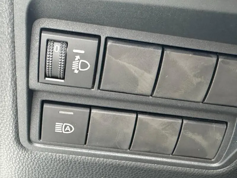 Détail des commandes intérieures noires avec réglage des phares sur Toyota Yaris 116h Dynamic 5p Blanc Lunaire 2025.