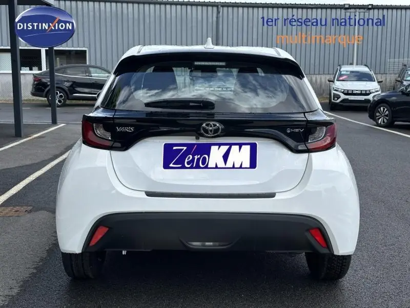 Vue arrière d'une Toyota Yaris 116h Dynamic blanche Lunaire avec détails noirs et feux arrière foncés, en stationnement extérieur.
