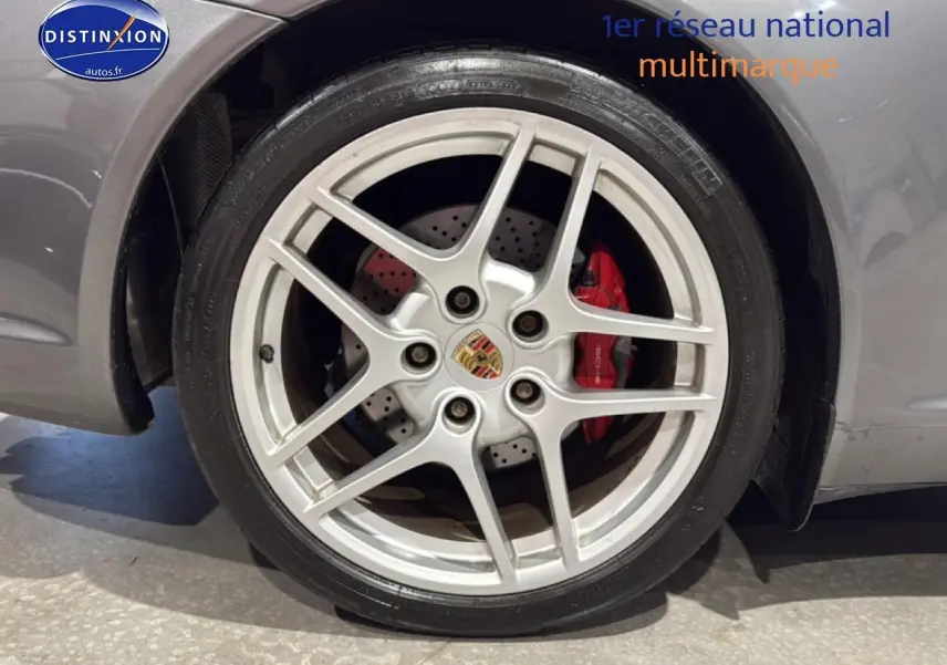 Gros plan sur la jante alu argentée avec logo Porsche et étrier de frein rouge d'une Porsche 911 gris.