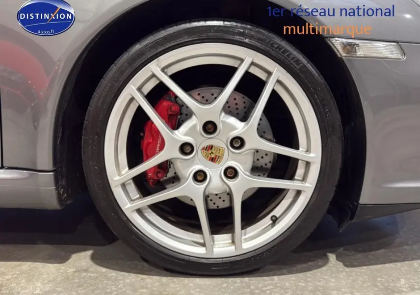 Gros plan sur la jante alu argentée et l’étrier de frein rouge du côté avant droit d’une Porsche 911 gris métallisé.