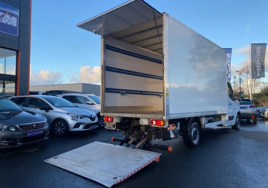 Vue 3/4 arrière d’un Renault Master blanc avec hayon élévateur déployé, montrant l’espace de chargement vide.