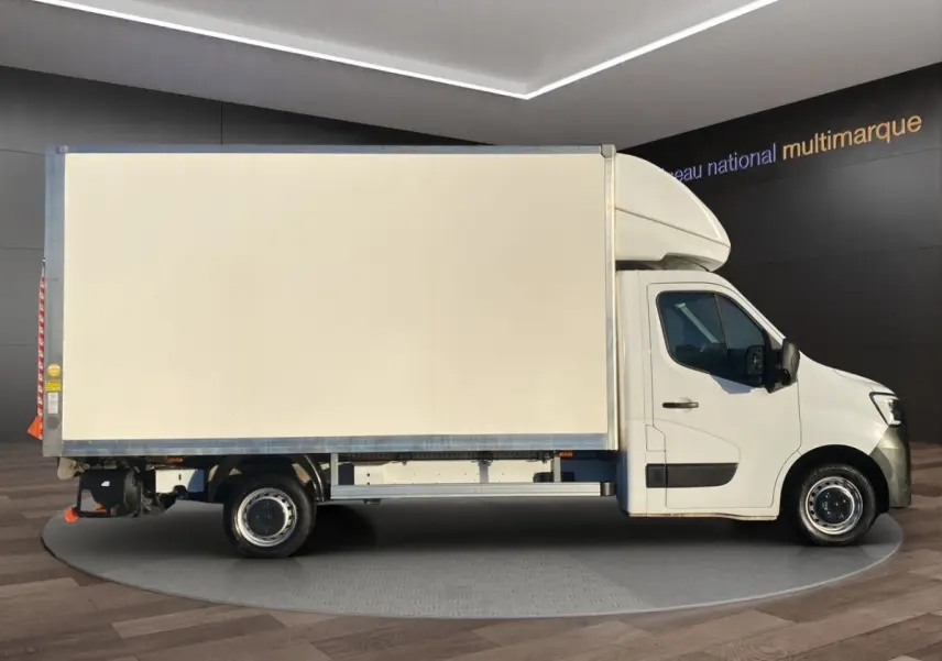 Vue latérale droite du Renault Master blanc avec caisse fermée et hayon, en intérieur showroom.