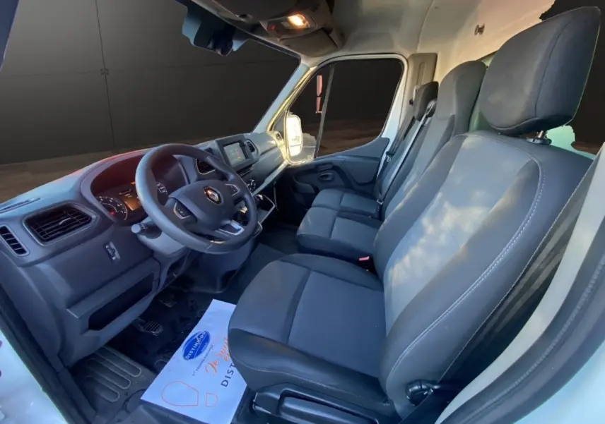 Vue intérieure côté conducteur du Renault Master blanc 2023, montrant le tableau de bord et les sièges avant gris foncé.