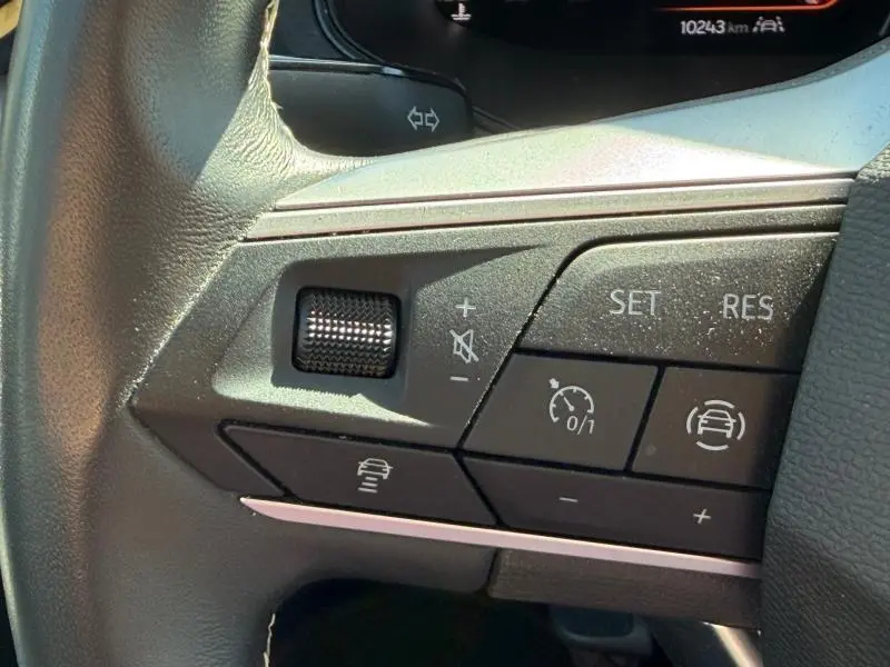 Gros plan sur les commandes du volant cuir noir du SEAT Arona 2025, boutons de régulateur de vitesse et volume sonore.