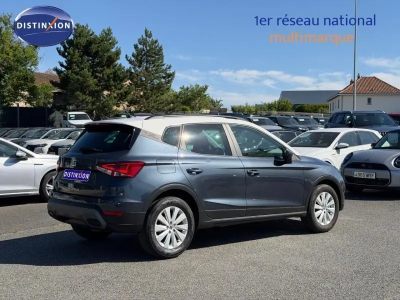 Vue 3/4 arrière droite d'une SEAT Arona 2025 gris magnétique métal avec toit blanc Candy sur parking.