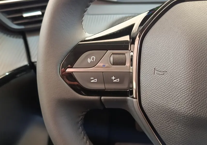 Gros plan sur les commandes gauche du volant cuir noir du Peugeot 208 électrique blanc 2024, avec boutons multifonctions.