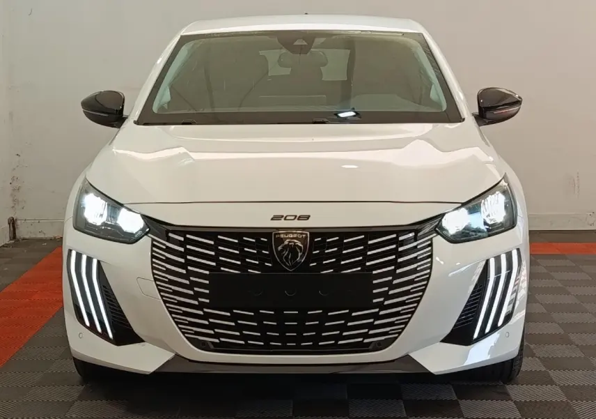 Vue frontale d'une Peugeot 208 électrique blanche 2024 avec phares LED et calandre noire distinctive.