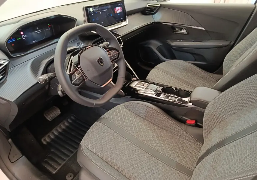 Vue intérieure côté conducteur de la Peugeot 208 électrique 2024, sièges gris et tableau de bord avec écran tactile.