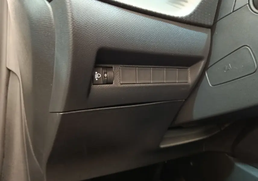 Détail intérieur côté conducteur du tableau de bord noir avec commande réglage hauteur phares Peugeot 208 électrique 2024.