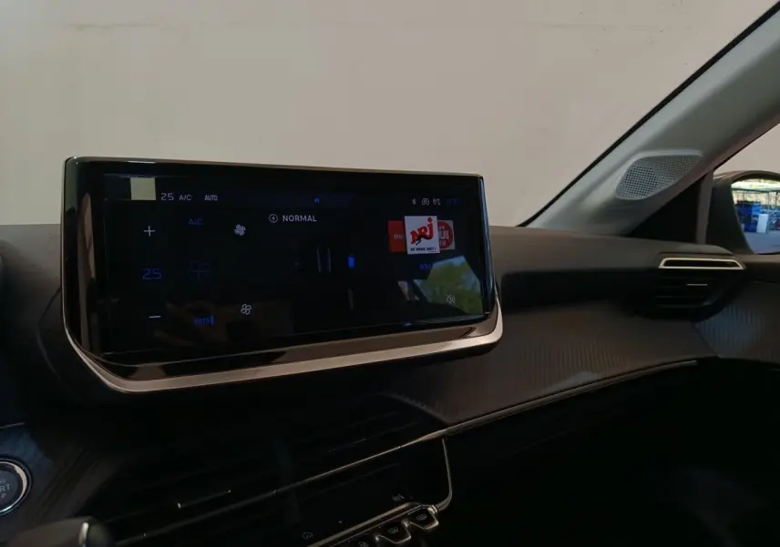 Vue intérieure du tableau de bord de la Peugeot 208 électrique 2024, avec écran tactile central et commandes climatisation digitales.