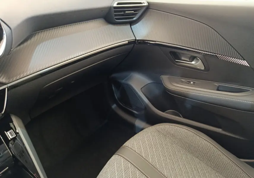 Vue intérieure côté passager du Peugeot 208 électrique 2024, montrant tableau de bord et siège gris texturé.