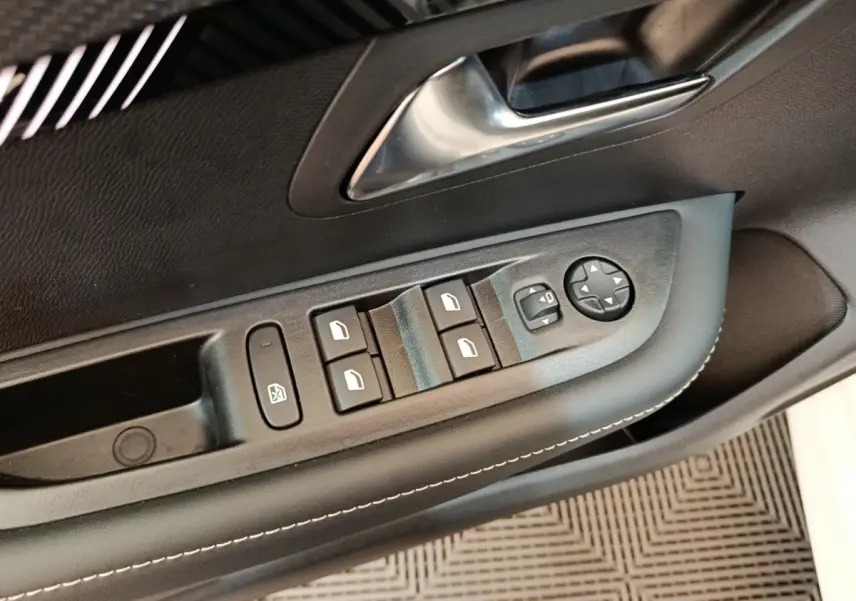 Gros plan sur la commande des vitres électriques et rétroviseurs côté conducteur d'une Peugeot 208 blanche de 2024.