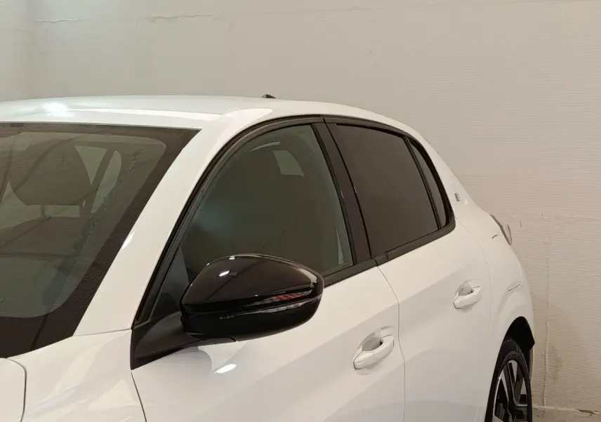 Vue 3/4 arrière gauche d'une Peugeot 208 électrique blanche avec rétroviseur noir et vitres teintées.