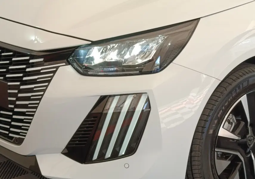 Gros plan sur l'avant droit blanc du Peugeot 208 électrique 2024, mettant en valeur les phares LED et la calandre distinctive.